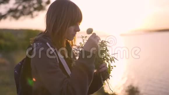 日落时分美丽的年轻女子带着一束野花在海岸上视频的预览图