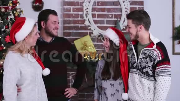 两对可爱的夫妇互相交谈和微笑展示肚子在圣诞树和壁炉周围视频的预览图