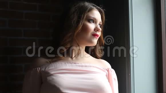穿着粉红色裙子的漂亮女孩透过窗户的肖像视频的预览图