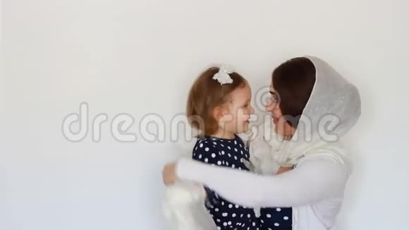 一位戴着头巾的年轻穆斯林妇女抱着一个婴儿母亲和女儿一起玩拥抱和亲吻她光线视频的预览图