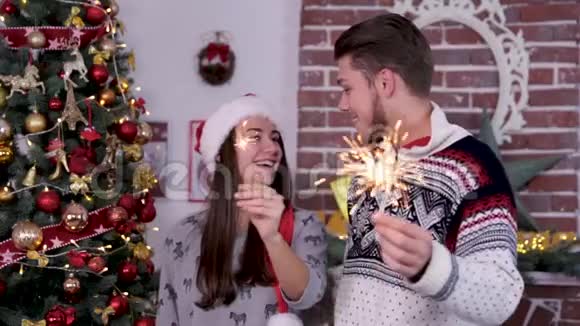 可爱的年轻夫妇带着有趣的圣诞老人红帽子拿着火花庆祝圣诞快乐视频的预览图