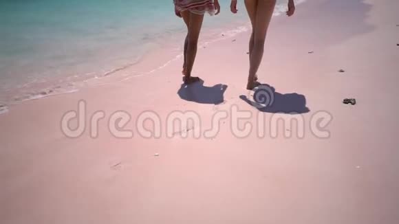 慢动作两个女孩踩着他们的脚印在粉红色的沙滩上把漂亮的晒黑的腿贴在粉红色的沙滩上视频的预览图