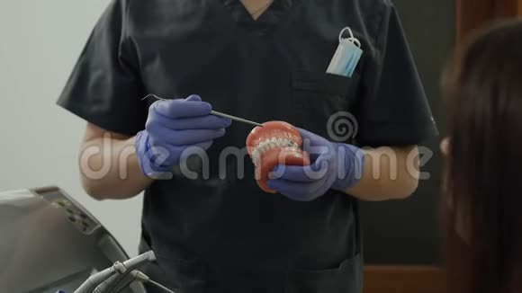 帅气的牙医在牙科诊所给一位拿着假牙的女病人做咨询牙科技师视频的预览图