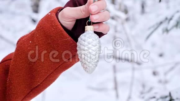 在一个真正的冬天里一只戴着手套的近距离雌性手把圣诞玩具挂在一棵白雪覆盖的树枝上视频的预览图