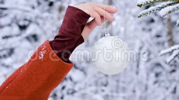 在一个真正的冬天里一只戴着手套的近距离雌性手把圣诞玩具挂在一棵白雪覆盖的树枝上视频的预览图