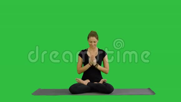 年轻女子练习瑜伽坐在莲花的位置闭着眼睛在绿色的屏幕上沉思Chroma键视频的预览图