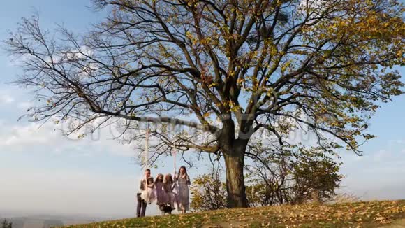 父亲和母亲在树下的秋千上摇动她的女儿视频的预览图