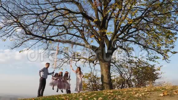 父亲和母亲在树下的秋千上摇动她的女儿视频的预览图