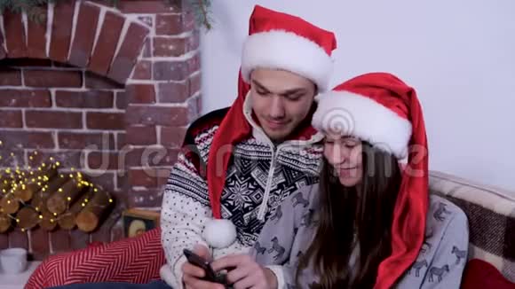 快乐的一对夫妇在壁炉前一起庆祝圣诞快乐在电话里看着一些东西视频的预览图