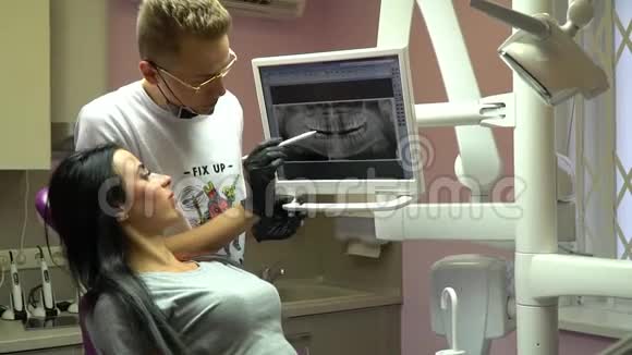 戴眼镜的牙医在屏幕上向病人显示牙齿的x光并描述情况视频的预览图