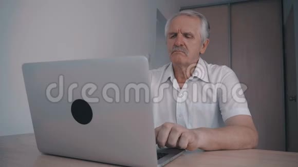 一位留着胡子的老人坐在桌子旁的办公室里手提电脑工作视频的预览图