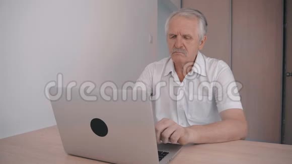 一位留着胡子的老人坐在桌子旁的办公室里手提电脑工作视频的预览图