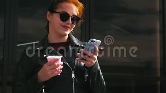 年轻的女人在街上喝咖啡打字发手机短信在城市里散步视频的预览图