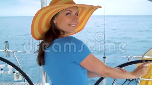穿着黄色帽子和蓝色裙子的女人站在游艇上在海洋的夏季微笑视频的预览图