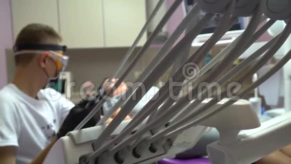 戴医用口罩的牙医正在给病人牙齿钻孔牙科办公室的一位黑发女子病人带紫色牙科的房间视频的预览图
