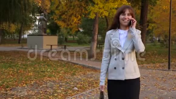 美丽的商务女性在手机上交谈快乐的女性在秋天公园散步微笑着视频的预览图