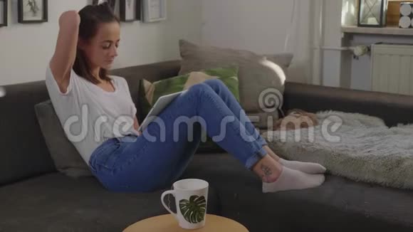 年轻女子端着平板电脑坐在沙发上视频的预览图