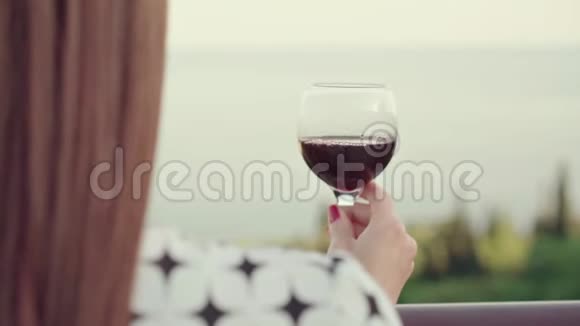 稚嫩的红发少女站在酒庄的露台上手里拿着一杯红酒女人喝葡萄酒可以欣赏大海视频的预览图