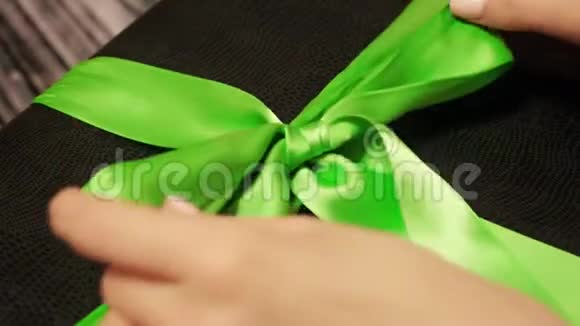 女士双手解开黑色礼盒上的绿色丝带木制桌子上放着一双柔软的女性手打开行李视频的预览图