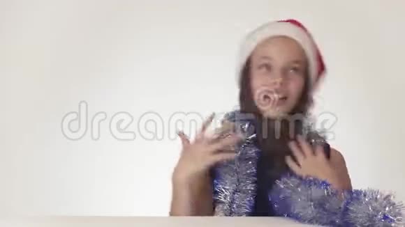 戴着圣诞老人帽子戴着新年礼物的美丽少女在白色的背景下快乐地调皮地跳舞视频的预览图