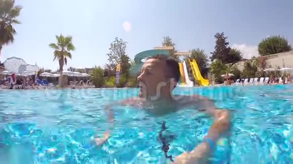 年轻人在水上公园的游泳池里游泳环顾四周他手里拿着相机做自画像关门视频的预览图