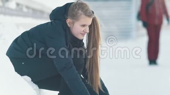坐在雪地上的十几岁长发女孩收紧了溜冰鞋的鞋带微笑着视频的预览图