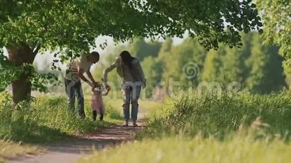 一个幸福的家庭父亲母亲和一个迷人的小女儿在森林公园里沿着小路跑牵着手夏季视频的预览图