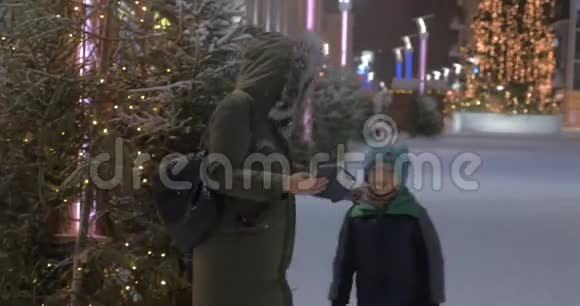 妈妈和孩子在街上用圣诞照明做冬天的自拍视频的预览图
