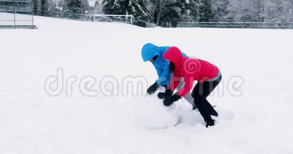 一对夫妇推着一个巨大的雪球视频的预览图