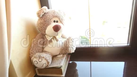 泰迪熊坐在窗台上可爱的泰迪熊靠近窗户脖子上有一只蝴蝶浅棕色孩子们视频的预览图