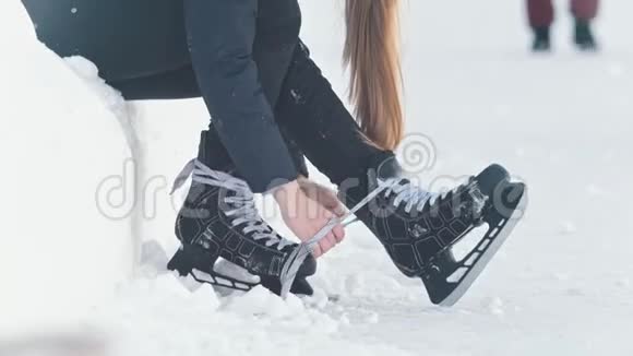 坐在雪地上的十几岁长发女孩收紧了溜冰鞋的鞋带微笑着视频的预览图