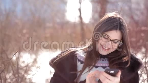 在白雪覆盖的地面上一个年轻的女孩使用一部手机纠正她的头发视频的预览图