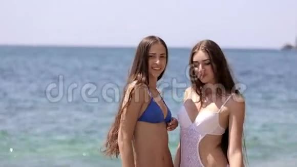 两个穿着比基尼的漂亮女孩站在海边诱人地移动视频的预览图
