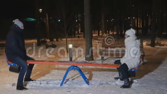 晚上冬季公园成年男女在跷跷板上摇摆视频的预览图