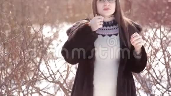 可爱的女孩戴着眼镜穿着貂皮大衣冬天在外面整理头发视频的预览图