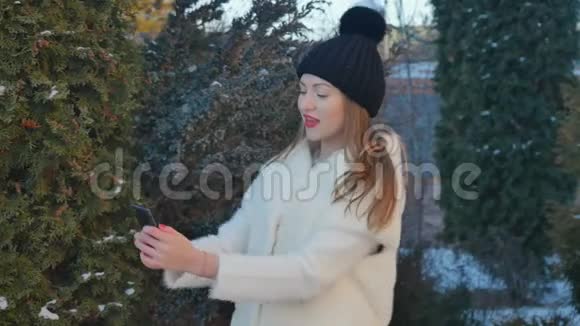 穿着白色毛皮外套的可爱女孩在杉树背景下自拍视频的预览图