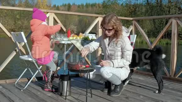 母亲和女儿一个年轻的女人和一个穿着温暖衣服的小女孩在烤架上准备蔬菜和肉使用视频的预览图