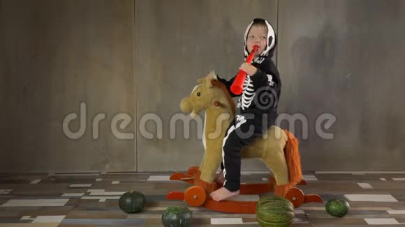 小男孩光着脚穿着骷髅服骑着摇摆玩具马儿童快乐庆祝万圣节手持南瓜形手电筒视频的预览图