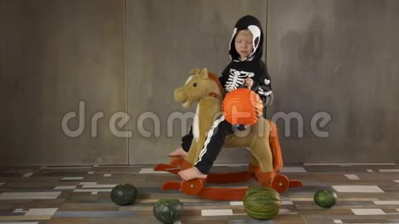 小男孩光着脚穿着骷髅服骑着摇摆玩具马儿童快乐庆祝万圣节手持南瓜形手电筒视频的预览图