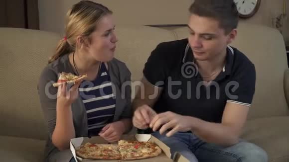 一对漂亮的年轻夫妇坐在沙发上吃披萨视频的预览图