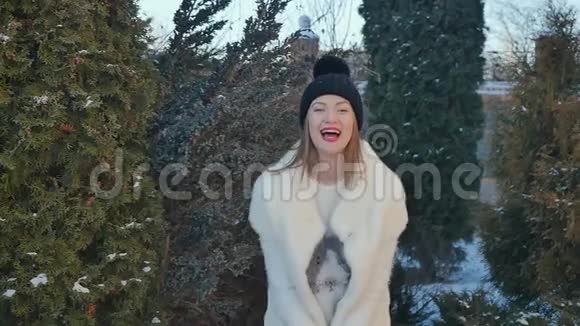 美丽的女孩把雪扔上来在冷杉的背景下为冬天而高兴视频的预览图
