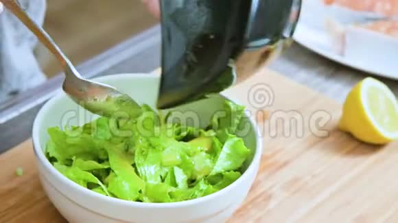 家庭厨房中的女性手的特写被添加到素叶沙拉酱中并在木制的勺子上混合视频的预览图
