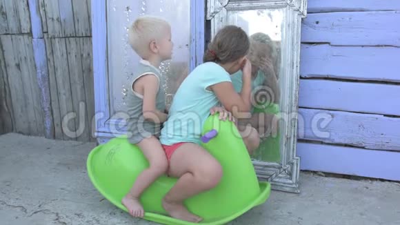 孩子们骑在绿色塑料马上在农村房子的院子里的镜子背景上摇摆漂亮的孩子视频的预览图
