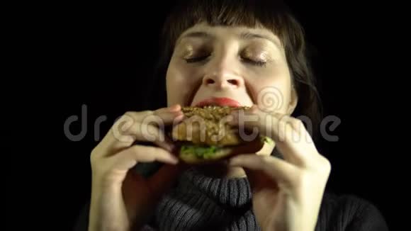 年轻女子在黑色背景下吃汉堡视频的预览图