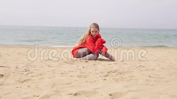 金发女孩坐在海边的沙滩上摆姿势拍照视频的预览图