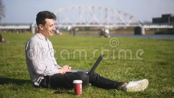 一个男人坐在公园里谈视频通讯一个学生一个自由职业者笑着笑着带笔记本的男人视频的预览图