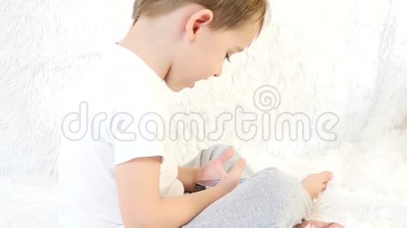一个孩子在玩智能手机坐在白色的背景上特写镜头视频的预览图