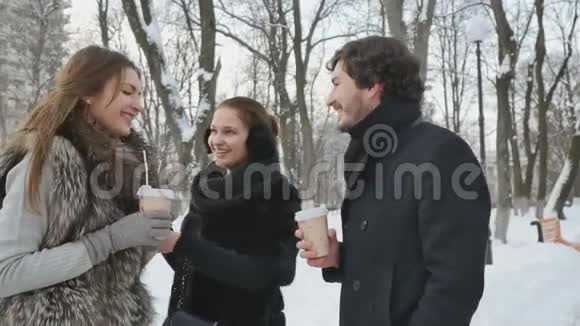 三个年轻朋友在冬季公园里聊天喝咖啡视频的预览图