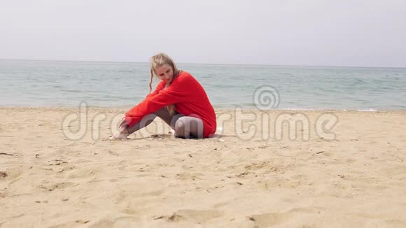 金发女孩坐在海边的沙滩上摆姿势拍照视频的预览图