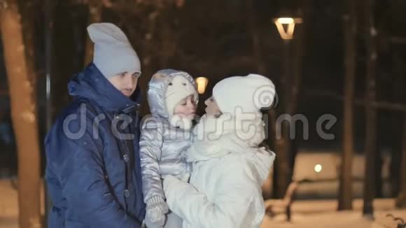 年轻夫妇与小女儿拥抱和亲吻的夜晚冬季公园视频的预览图